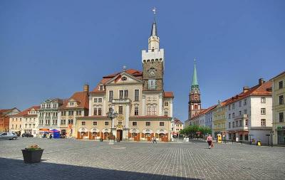Der Altmarkt in Löbau, Oberlausitz. Alte Gebäude, darunter zwei Türme. Im Vordergrund ein gepflasterter Platz.