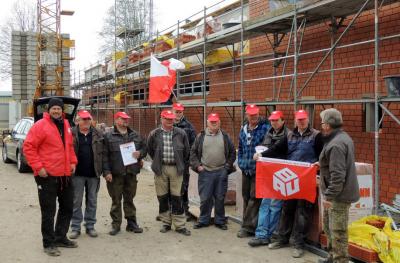 Bauleute mit IG BAU-Fahnen vor einem Rohbau mit Verblend-Arbeiten