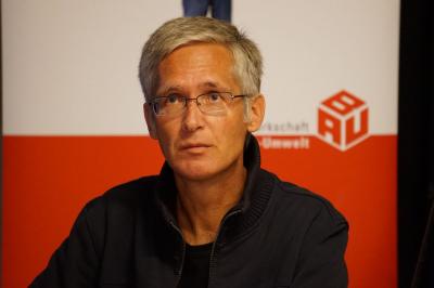 Grauhaariger Mann dunklem Teint und Brille, im Hintergrund der "BAU"-Würfel der IG BAU. Grauhaariger Mann dunklem Teint und Brille, im Hintergrund der "BAU"-Würfel der IG BAU.