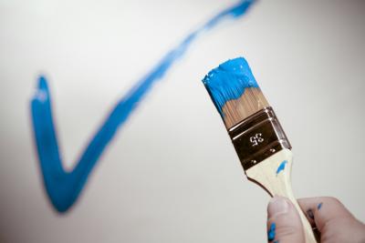 Pinsel mit blauer Farbe, blauer Haken auf weißer Wand