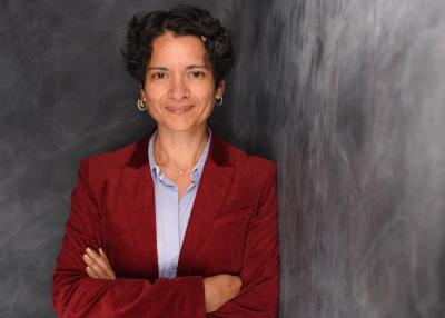 Tanja Chawla in rotem Oberteil vor einer grauen Wand.