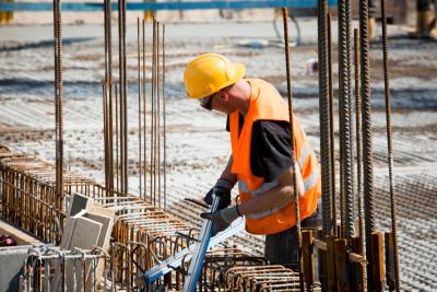 Bauarbeiter mit Warnweste zwischen Bewehrungsstählen auf einem Neubau.