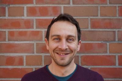 Portraitaufnahme von Alexander Kahl vor einer gemauerten Wand.