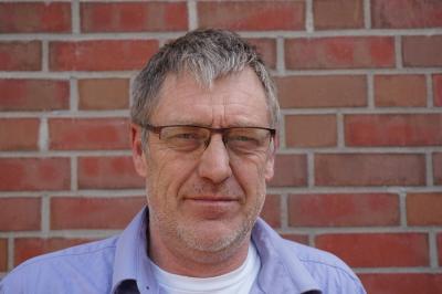 Portraitaufnahme Achim Bartels vor einer gemauerten Wand Portraitaufnahme Achim Bartels vor einer gemauerten Wand