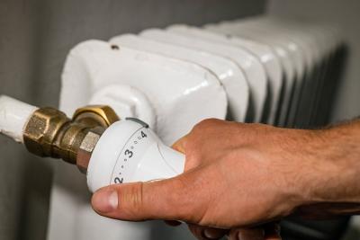 Eine Hand dreht an einem Heizungsthermostat.