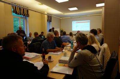 Etwa 20 Personen in einem Tagungsraum, die auf eine Projektion an der Wand blicken. Etwa 20 Personen in einem Tagungsraum, die auf eine Projektion an der Wand blicken.