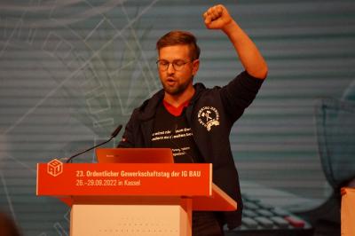 Redner "Cirka" von der Jungen BAU mit erhobener linker Faust am Rednerpult des Gewerkschaftstages