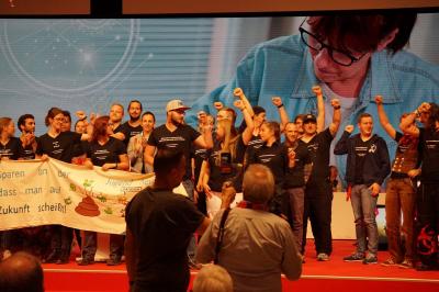 ca. 20 junge Gewerkschafter*innen auf der Bühne des Gewerkschaftstages. Alle tragen schwarze T-Shirts mit Slogans in weißer Schrift. Zwischen ihnen ein Transparent mit der Aufschrift "Sparen an der Jugend heißt, dass man auf die Zukunft scheißt."