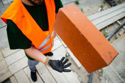 Kaminroter Ziegelstein zentral im Bild, hochgeworfen von einem jungen Mann in Warnweste mit schwarzem Handschuh. Kaminroter Ziegelstein zentral im Bild, hochgeworfen von einem jungen Mann in Warnweste mit schwarzem Handschuh.