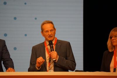 Harald Schaum, im grauen Anzug und weißem Hemd am Mikro. Harald Schaum, im grauen Anzug und weißem Hemd am Mikro.