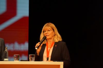 Ulrike Laux am Mikro, in schwarzem Jackett und weißem Hemd, um den Hals den Delegiertenausweis am roten Band. Ulrike Laux am Mikro, in schwarzem Jackett und weißem Hemd, um den Hals den Delegiertenausweis am roten Band.