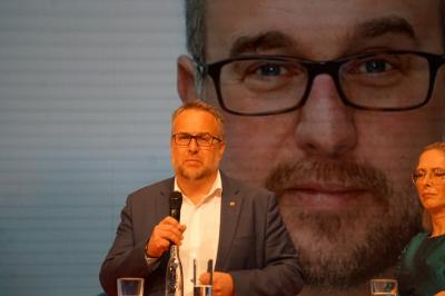 Carsten Burckhardt, in grauem Jackett und weißem Hemd vor einem überdimensionalen Foto von sich auf der Leinwand. Rechts neben ihm Nicole Siems im grünen Kleid. Carsten Burckhardt, in grauem Jackett und weißem Hemd vor einem überdimensionalen Foto von sich auf der Leinwand. Rechts neben ihm Nicole Siems im grünen Kleid.