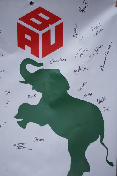 Ein auf ein Bettlaken gemalter, grüner Elefant, der sich aufrichtet, über ihm ein rotes BAU-Logo. Ein auf ein Bettlaken gemalter, grüner Elefant, der sich aufrichtet, über ihm ein rotes BAU-Logo.